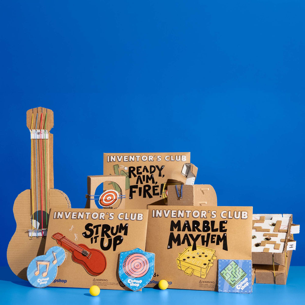 Chompshop Inventor's Club monthly project packs including Strum It Up, Ready Aim Fire, and Marble Mayhem cardboard building kits for kids to partner with the ChompSaw.