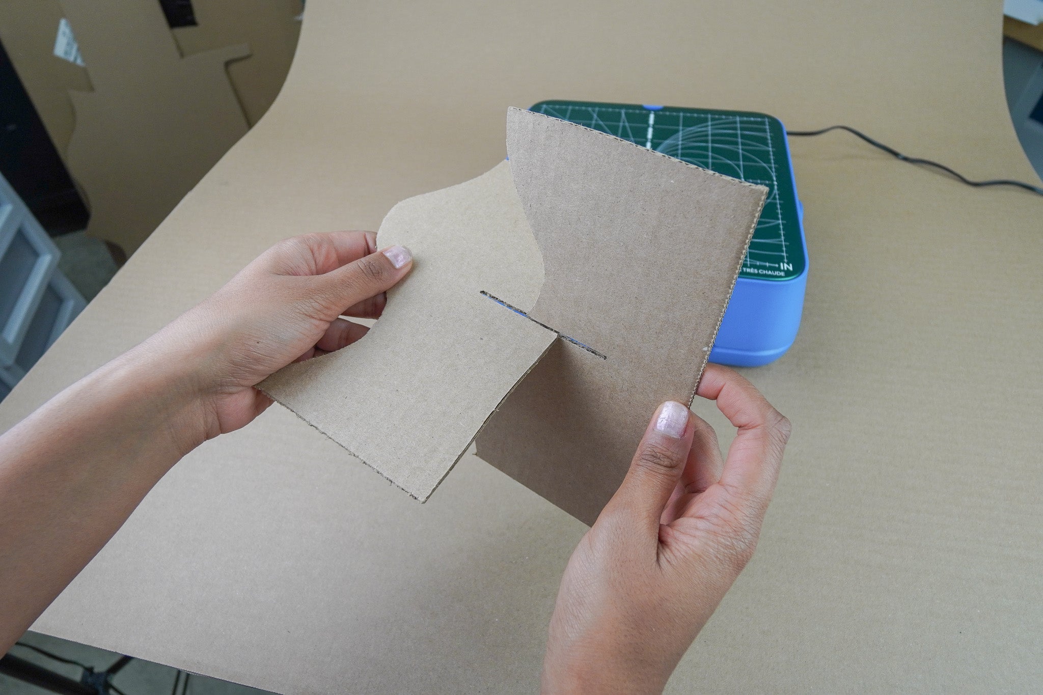 Two pieces of cardboard being slotted together along a cut line, to demonstrate that the width of cardboard cut is perfect for creating sturdy slots and tabs. ChompSaw by ChompShop in the background.