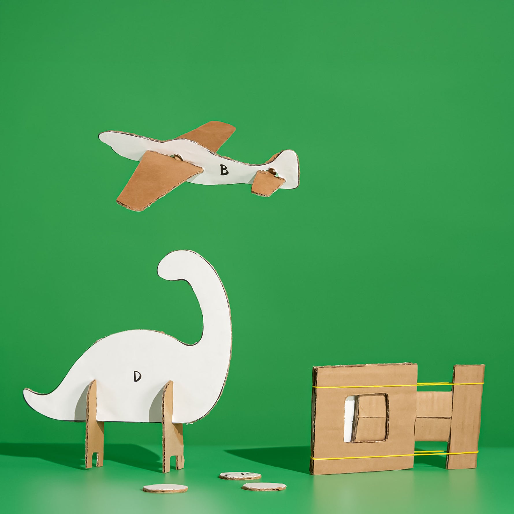 Cardboard dinosaur, airplane, and catapult made with the ChompSaw kids power tool on a green background.
