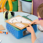 Child using the ChompSaw kids power tool to cut cardboard shapes at a table.