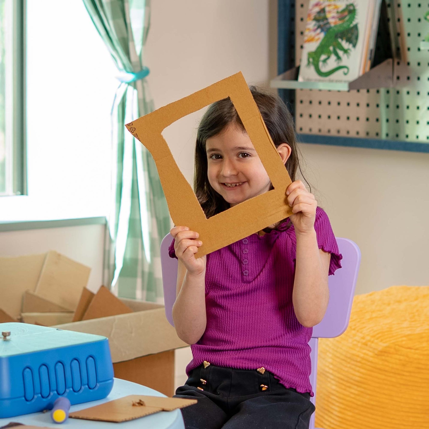 Young maker holding a cardboard picture frame she built using the Chompshop Hole Punch tool.