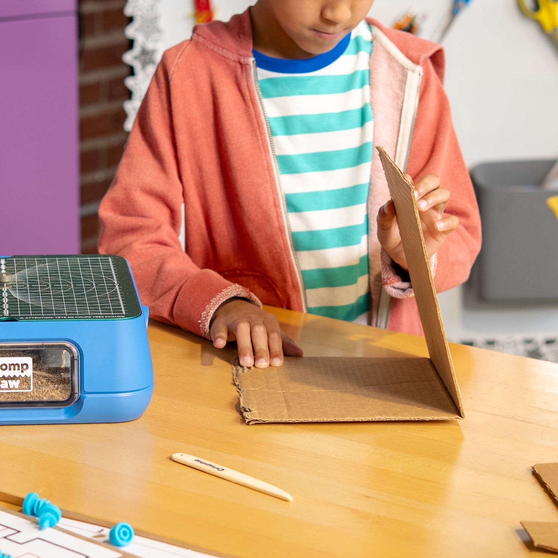 Child folding cardboard in a classroom setting after using Chompshop's Scoring Tool accessory.