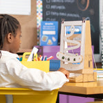 A young maker sits at a classroom desk, focused on a handmade cardboard snake game built with the ChompSaw from Chompshop's pattern templates. 