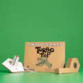 A cardboard toy kit labeled 'TOYS & GAMES Turbo Top' stands on a green surface against a solid green background.